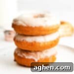 Three perfectly glazed old-fashioned doughnuts stacked on top of one another, set atop a pristine white plate, showcasing their inviting texture and sweet coating.