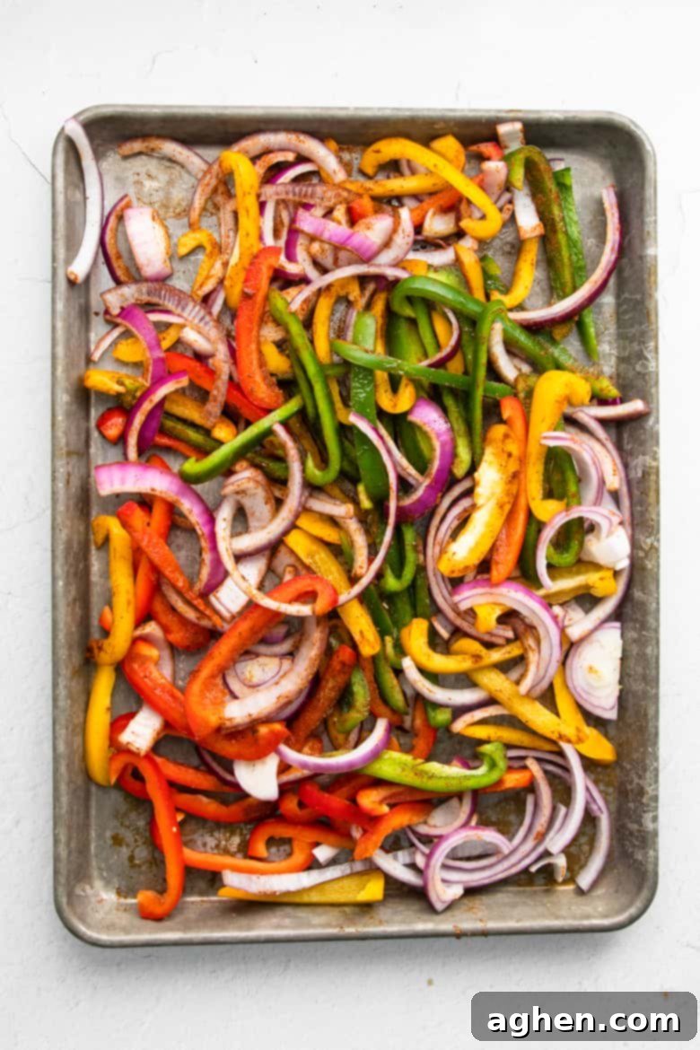 Easy Sheet Pan Shrimp Fajitas 5 Sliced bell peppers and red onions spread out evenly on a sheet pan, drizzled with olive oil and seasoning, ready for roasting.