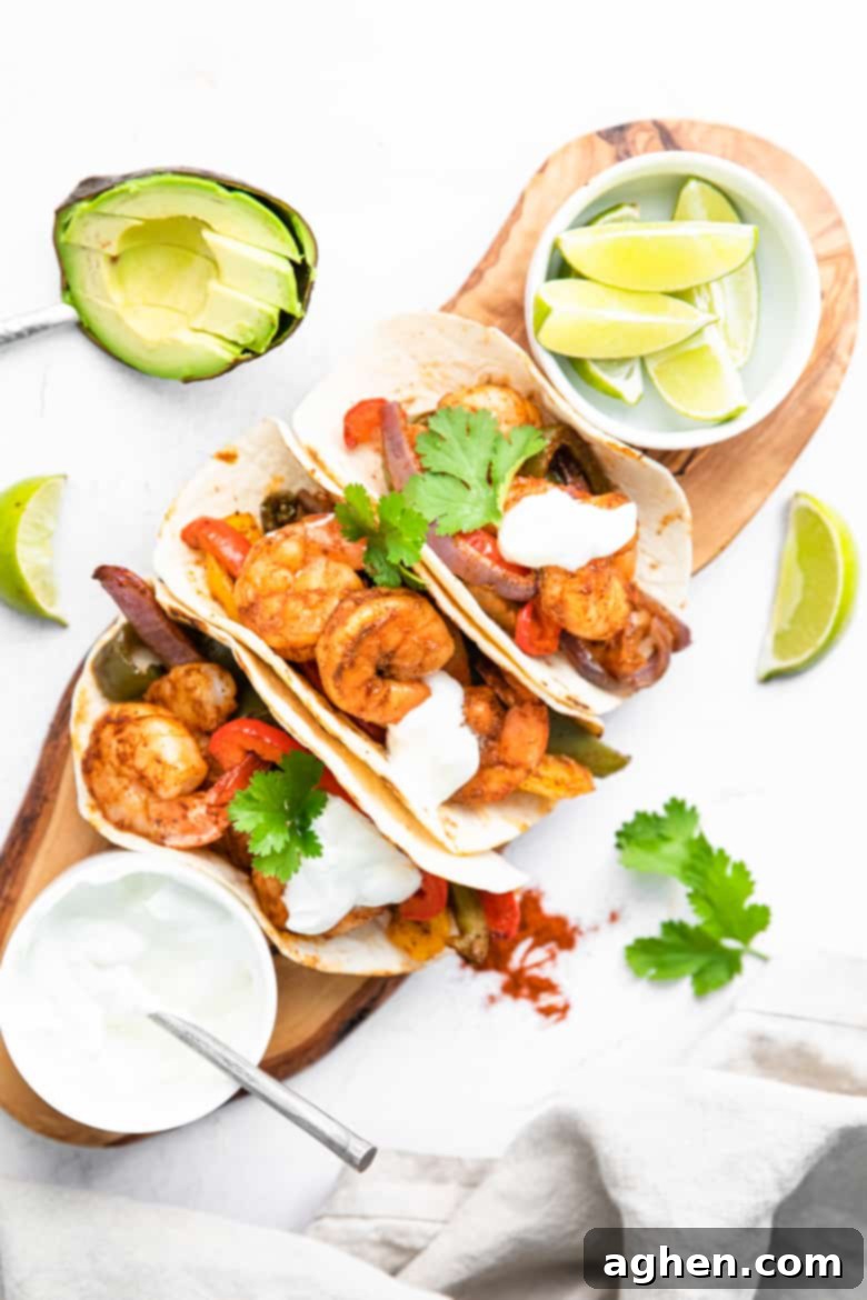 Easy Sheet Pan Shrimp Fajitas 7 Prepared shrimp fajitas beautifully plated, topped with fresh cilantro and a dollop of sour cream, served alongside lime wedges and sliced avocado for garnish.