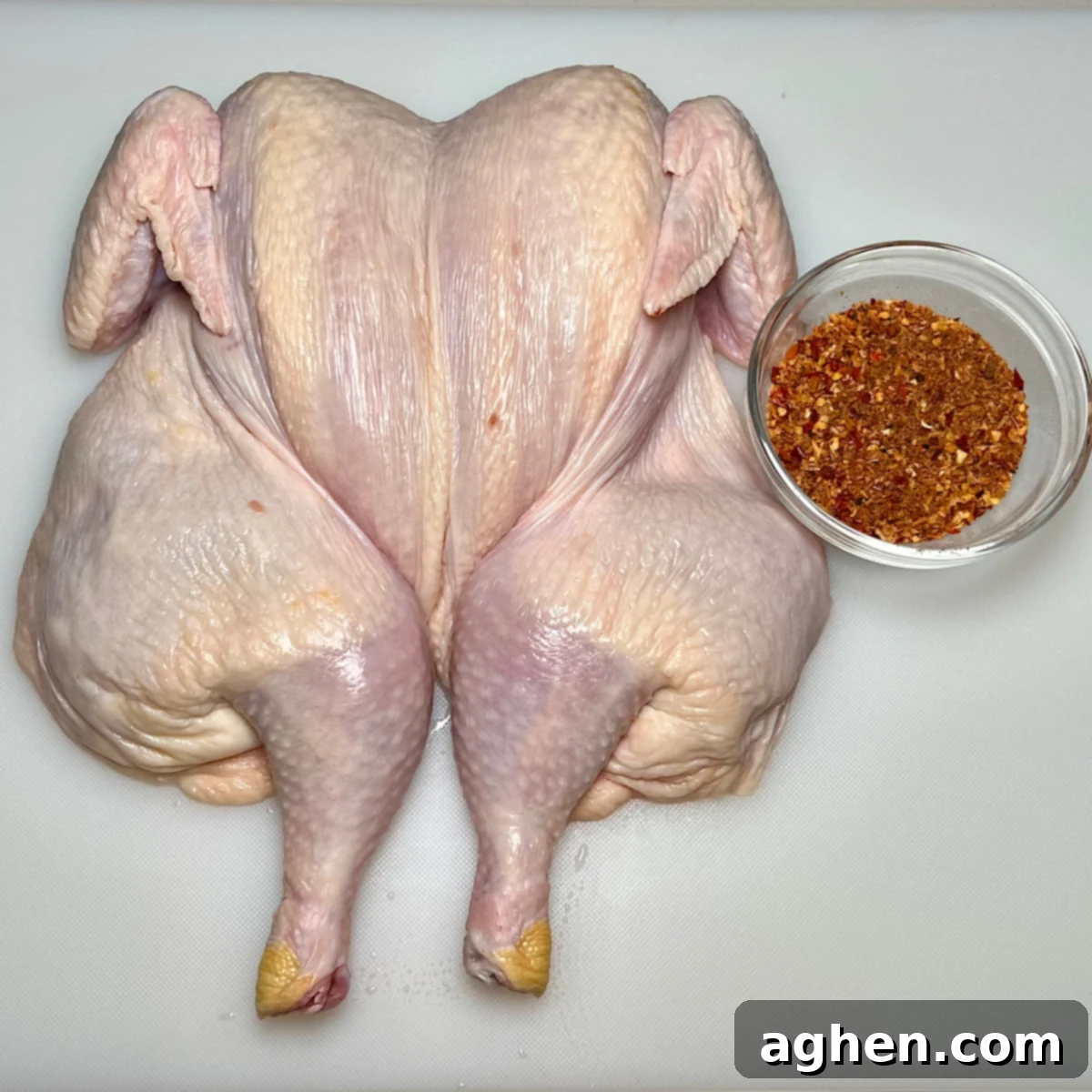 A whole spatchcock chicken thoroughly coated with a generous layer of chicken rub, ready for grilling.