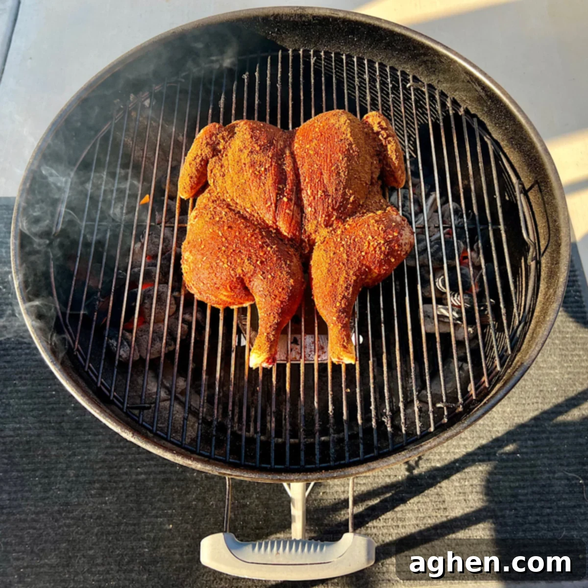 A raw, seasoned spatchcock chicken placed in the center of a Weber Kettle grill grate, positioned over indirect heat.