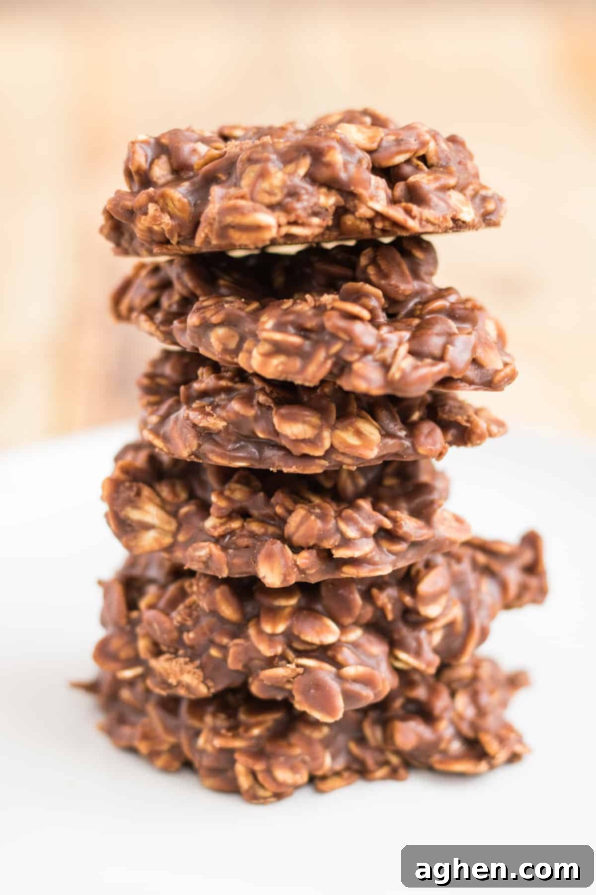 Six thick chocolate peanut butter oatmeal no bake cookies stacked one on top of another on a white plate.