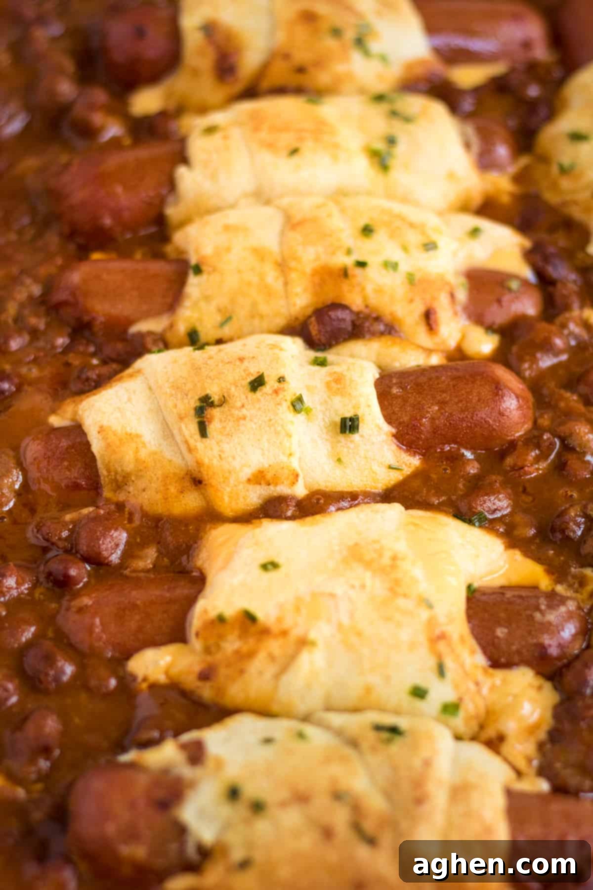 Chili cheese dog casserole made with hot dogs wrapped in cheese and crescent rolls and surrounded by chili