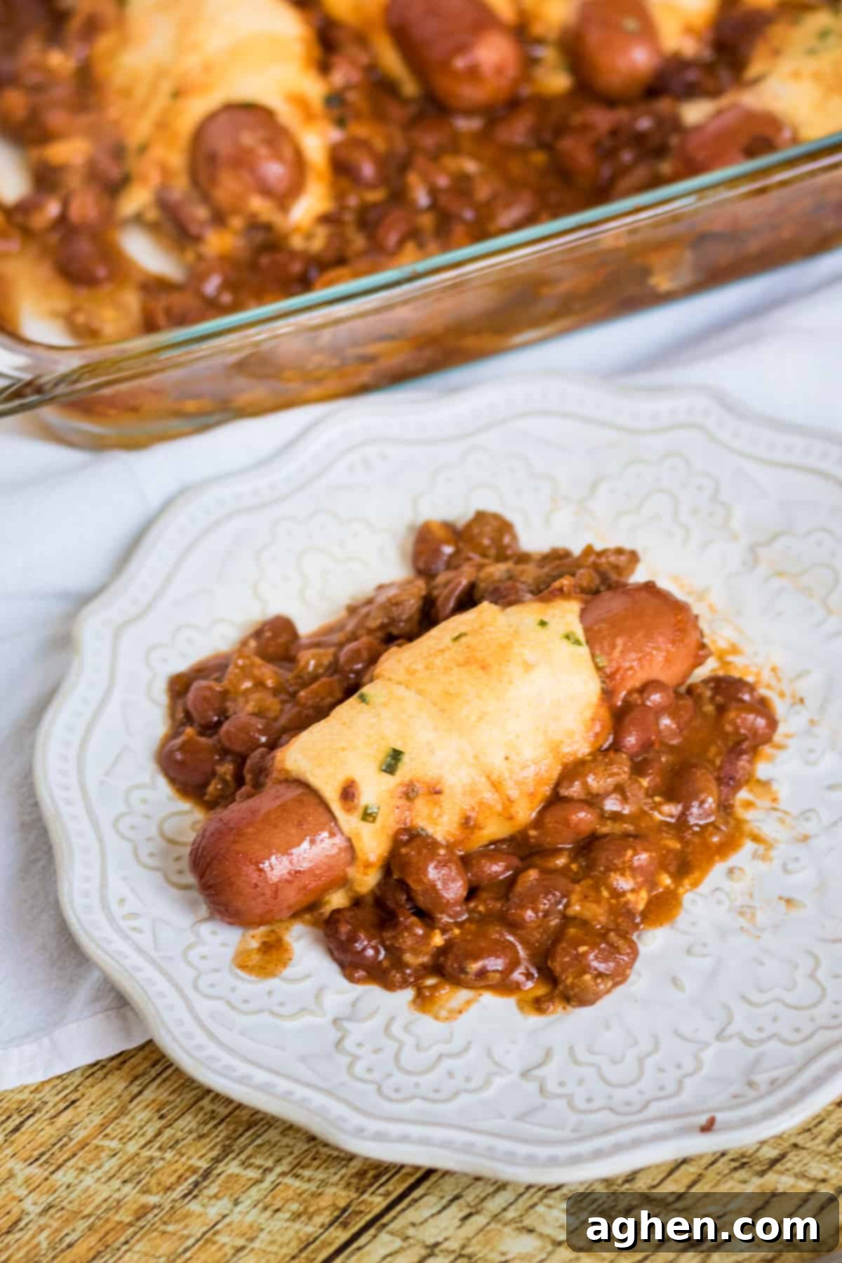 one chili cheese crescent hot dog on plate with casserole in background