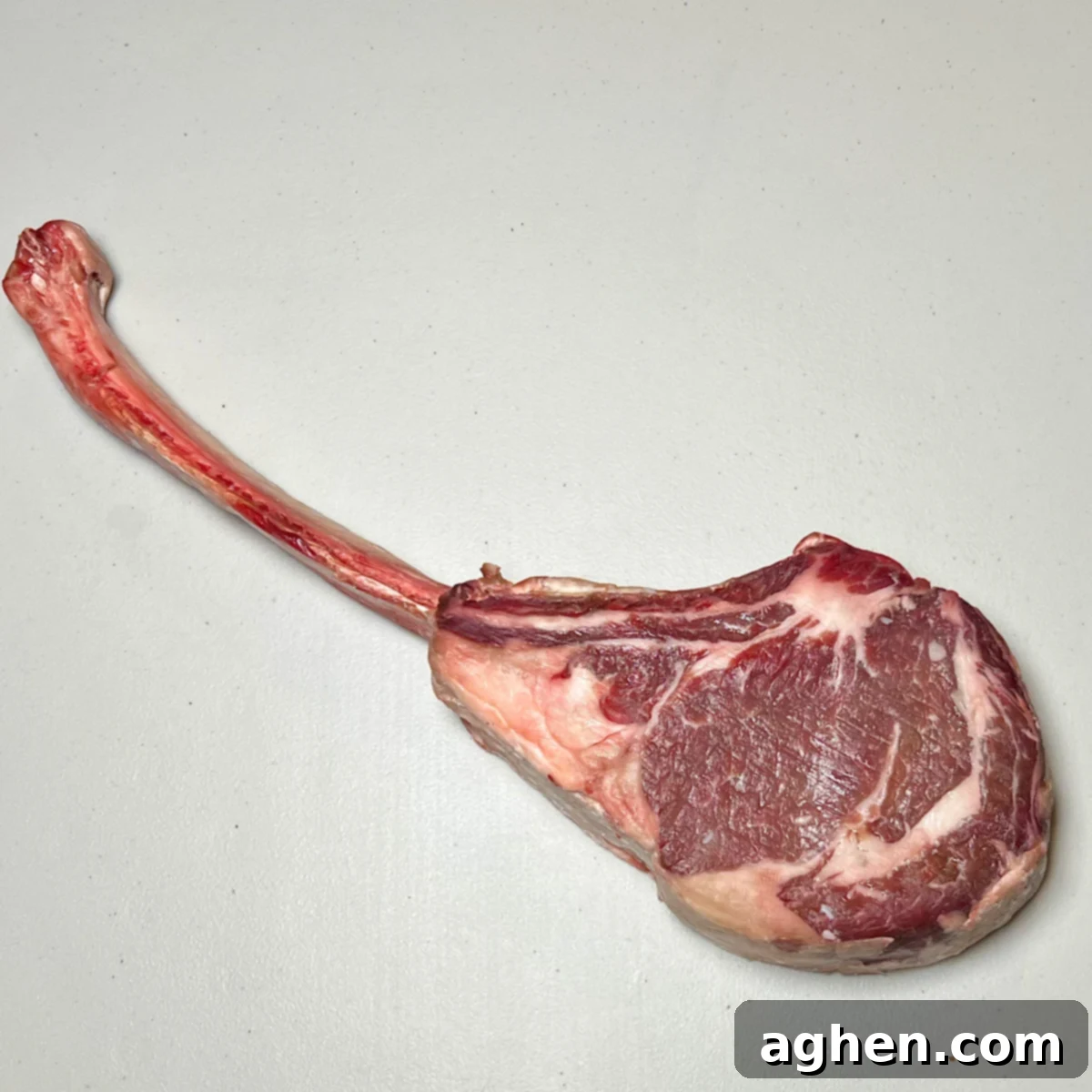 Raw, unseasoned tomahawk steak with its long bone, ready for preparation.