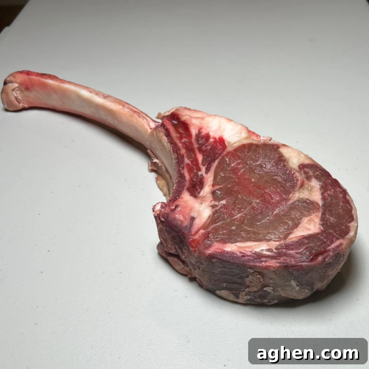 Raw tomahawk steak generously seasoned with olive oil, salt, and pepper.
