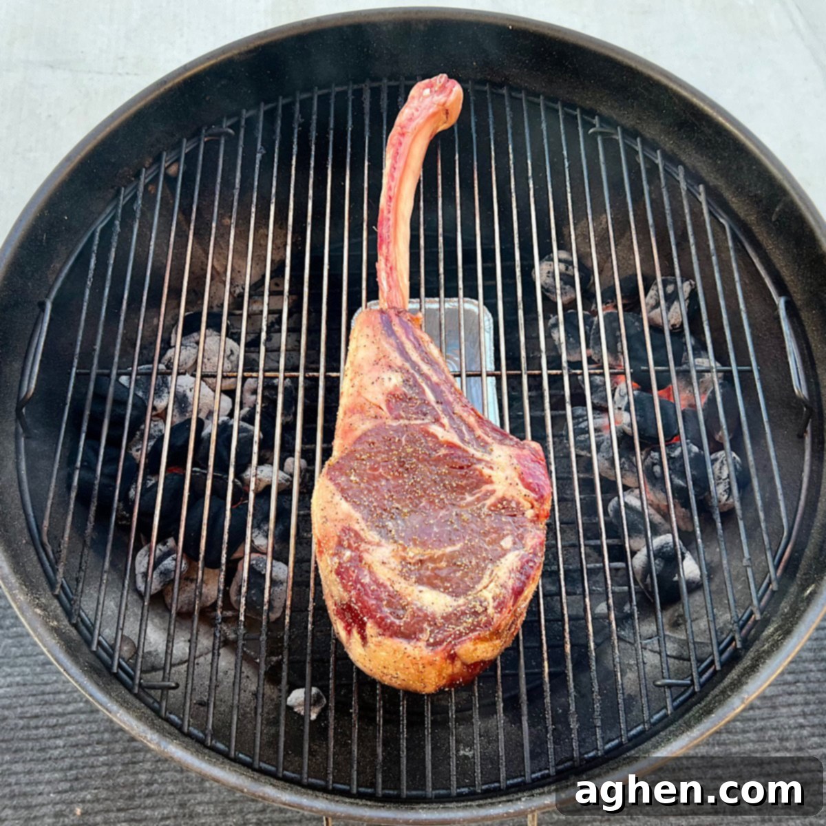 Raw tomahawk steak placed on the center of a Weber Kettle grill grate for indirect cooking.