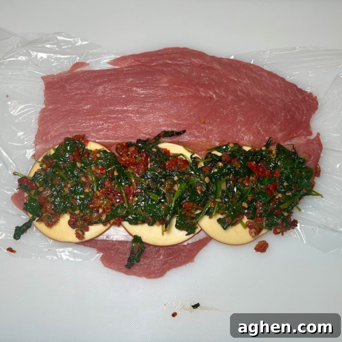 Pounded pork tenderloin with stuffing layered on top, ready to be rolled.