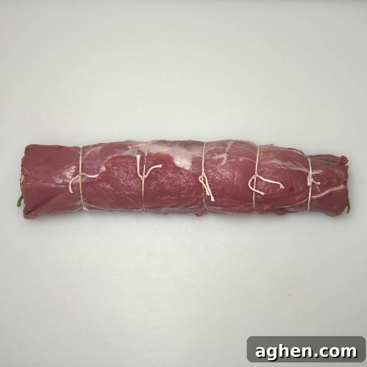 Rolled and tied finished pork tenderloin, ready for the grill, showcasing its neat cylindrical shape.