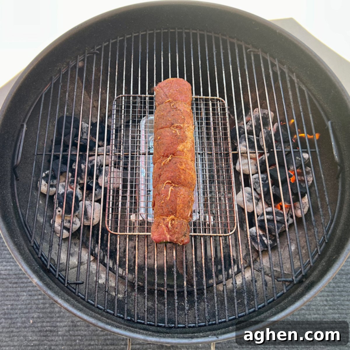 Raw, rolled, and stuffed pork tenderloin placed in the center of a Weber Kettle grill grate, positioned for indirect smoking.