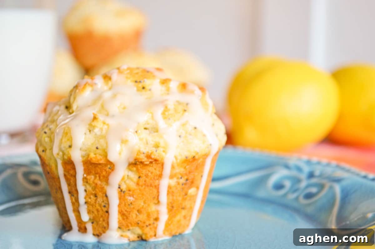 A perfectly baked lemon poppy seed muffin, generously drizzled with a bright lemon glaze that beautifully drips down its sides. In the softly blurred background, more muffins and two vibrant whole lemons complete the inviting scene, highlighting the freshness and appeal of these homemade treats.