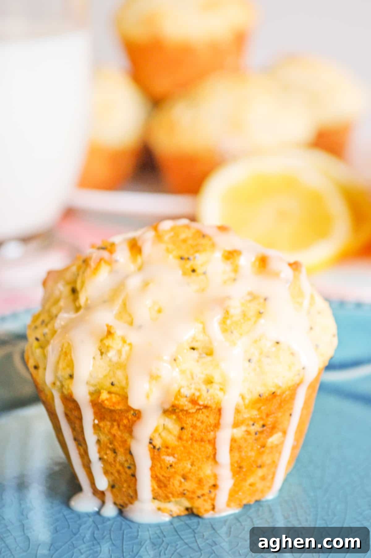 A close-up of a lemon poppy seed muffin, lavishly drizzled with a sweet lemon glaze cascading down its sides. In the background, more freshly baked muffins and artfully sliced lemons create an appetizing display, emphasizing the fresh ingredients and delicious outcome.
