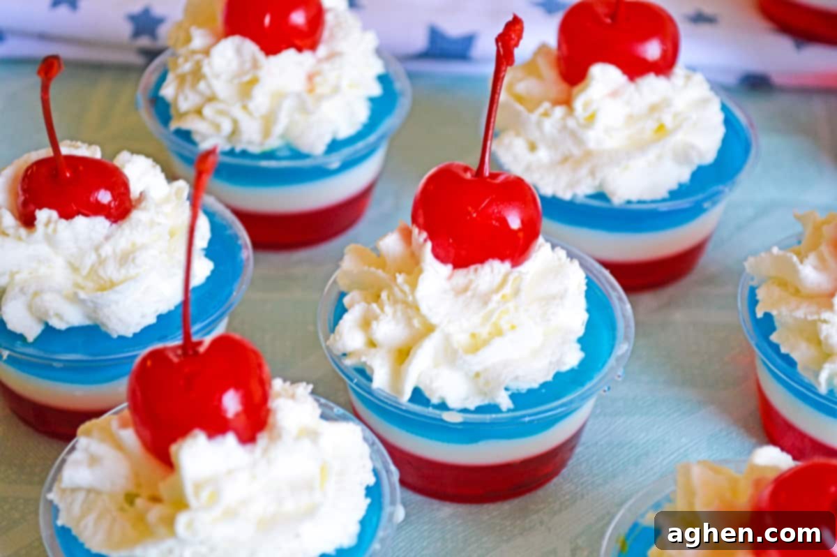 several red, white, and blue jello shots topped with whipped cream and cherries in small disposable plastic cups.