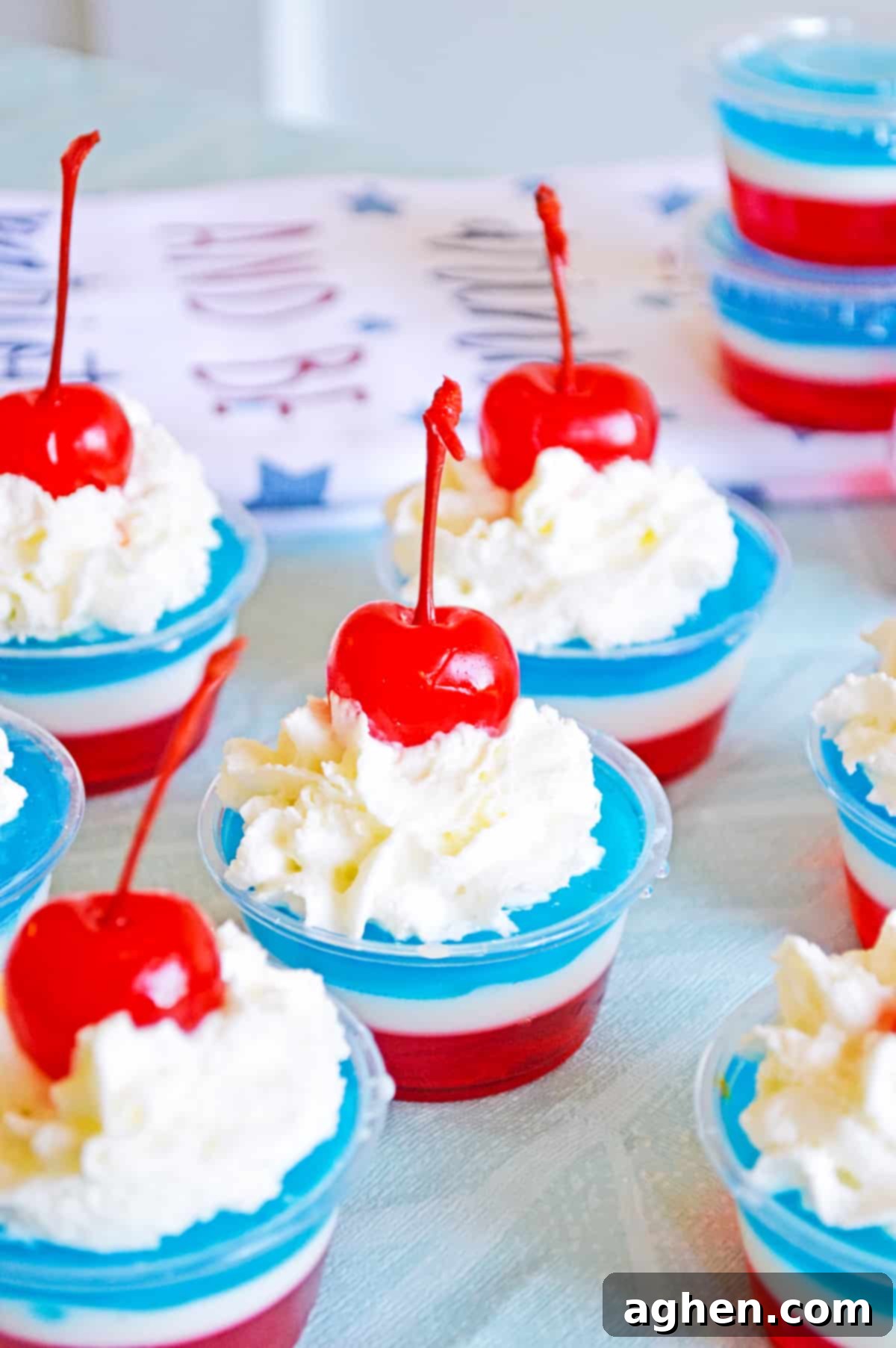 several red, white, and blue jello shots topped with whipped cream and cherries in small disposable plastic cups.