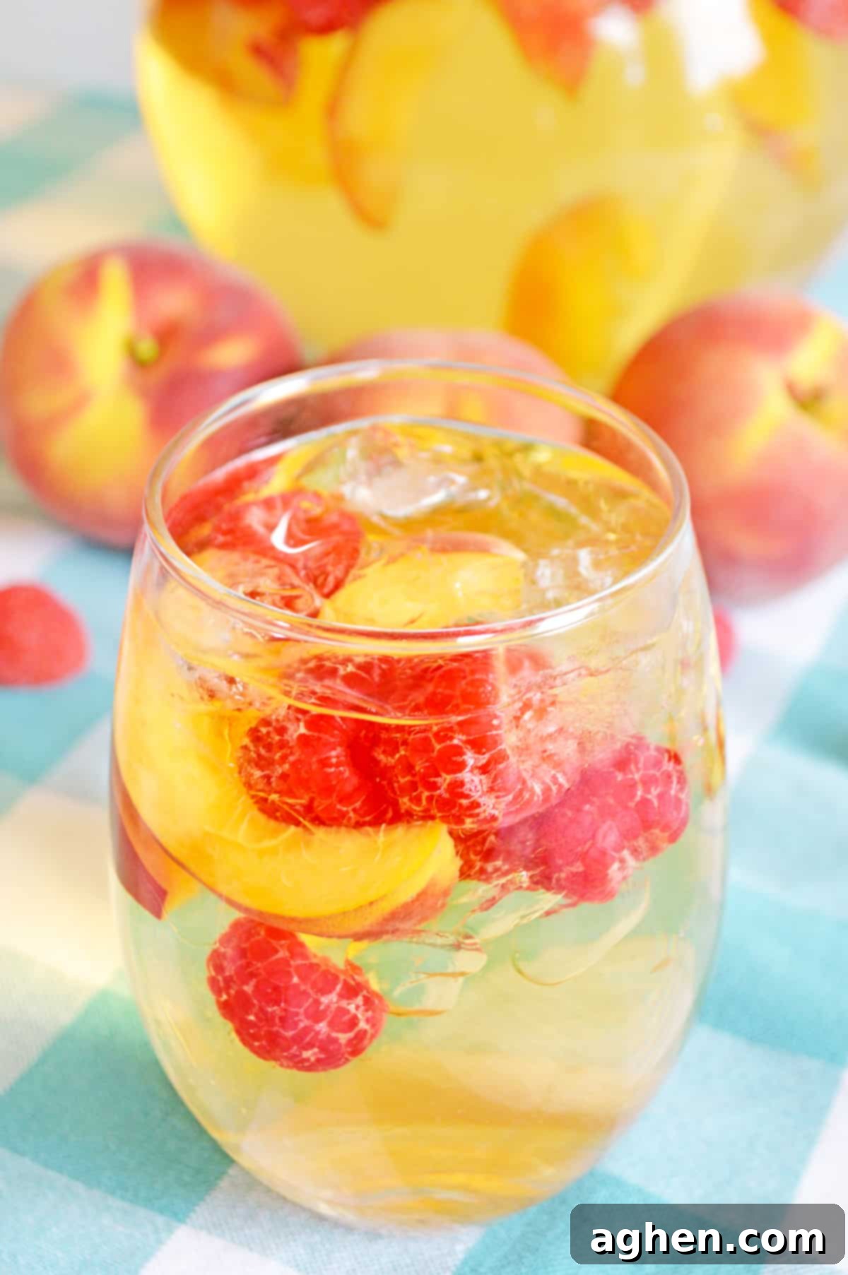 Refreshing Peach Sangria 3 White sangria with peaches and raspberries in wine glass with pitcher and fresh fruit in background