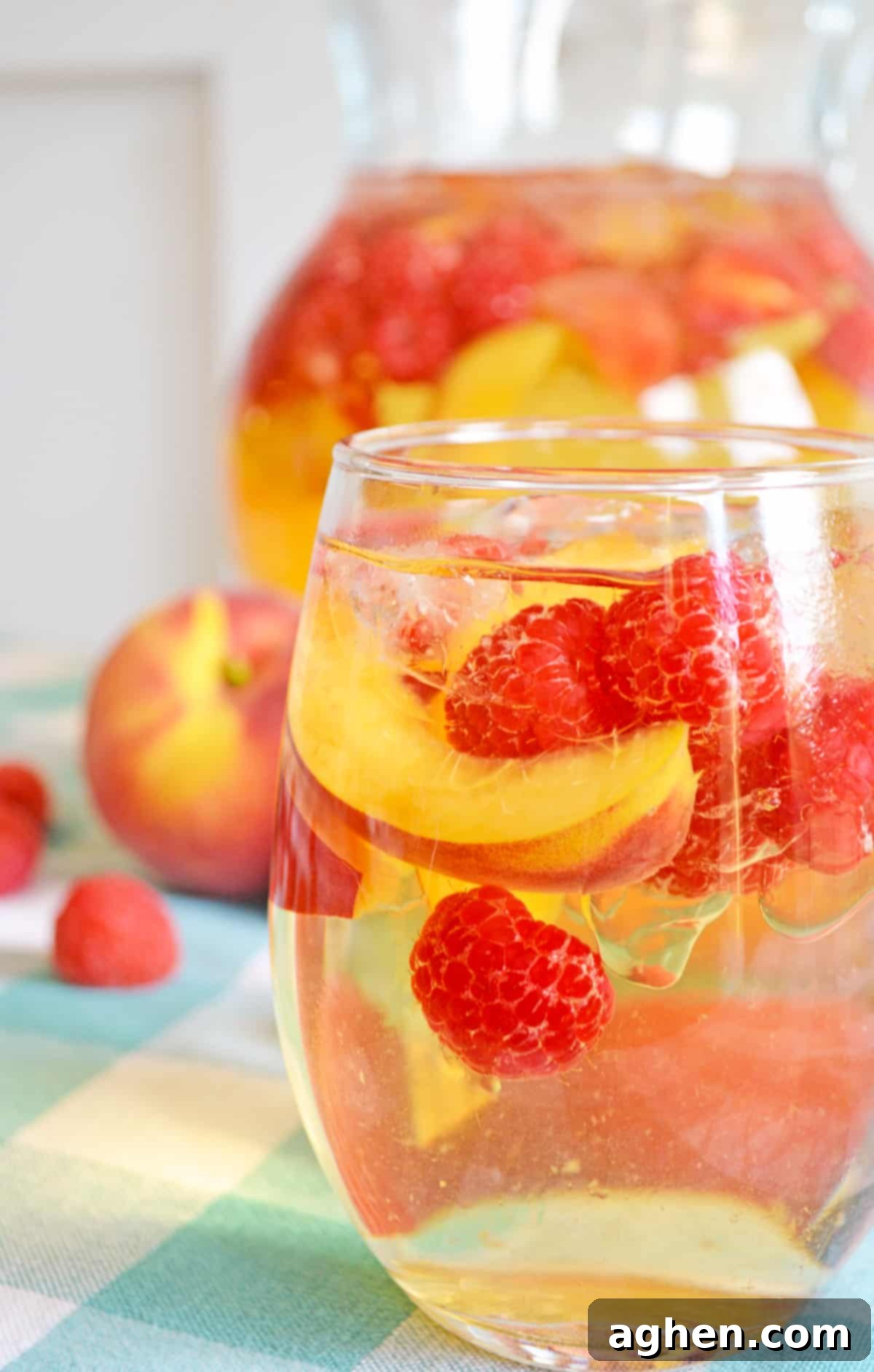 Refreshing Peach Sangria 4 White peach sangria with fresh raspberries and peaches. Pitcher full of sangria and more fresh fruit in background.
