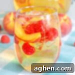 Refreshing Peach Sangria 6 White peach sangria with fresh peaches and raspberries in a stemless wine glass with whole peaches in background