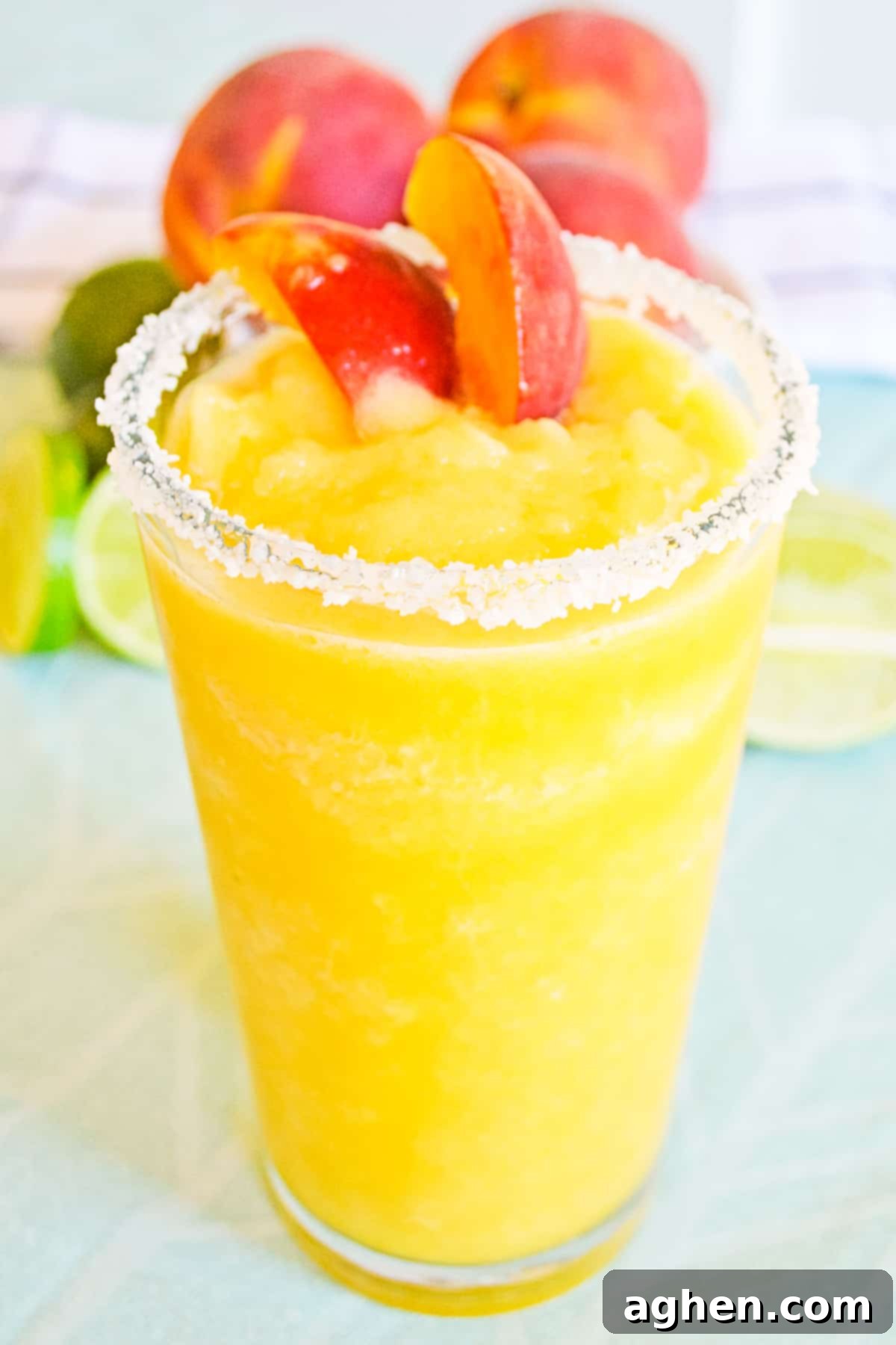 Frozen Peach Cocktail in glass with salt rim and garnished with fresh peaches, ready for summer enjoyment.