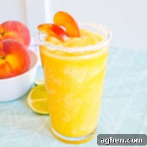 Frozen peach margarita with salt rim and garnish of fresh peach slices