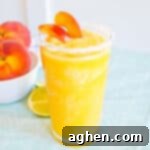 Frozen peach margarita with salt rim and garnish of fresh peach slices