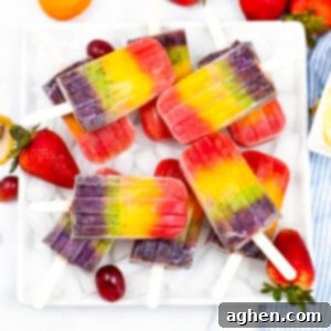 Rainbow popsicles served on a white platter garnished with strawberries and grapes