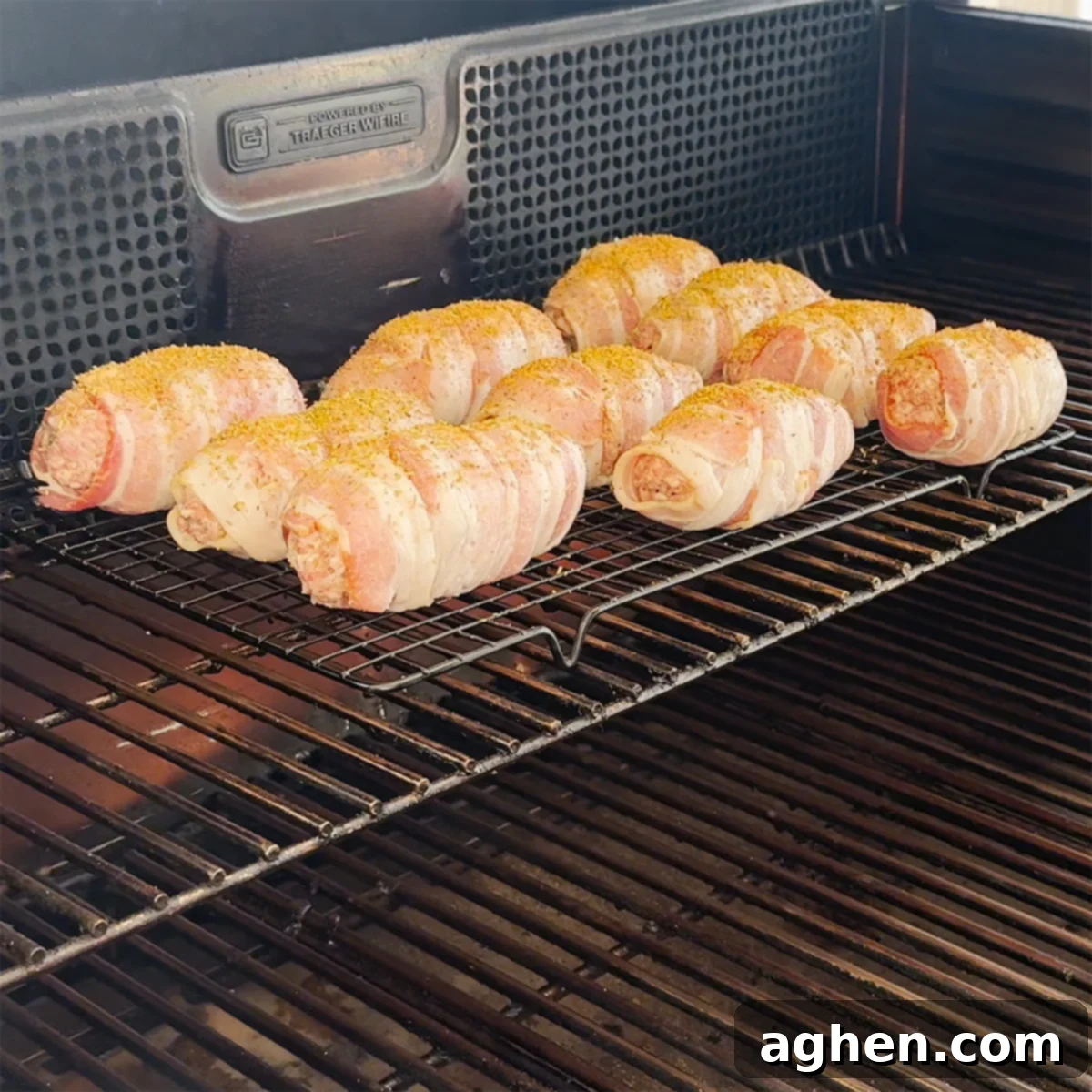 Bacon-Wrapped Armadillo Eggs smoking on a wire rack inside a pellet grill.