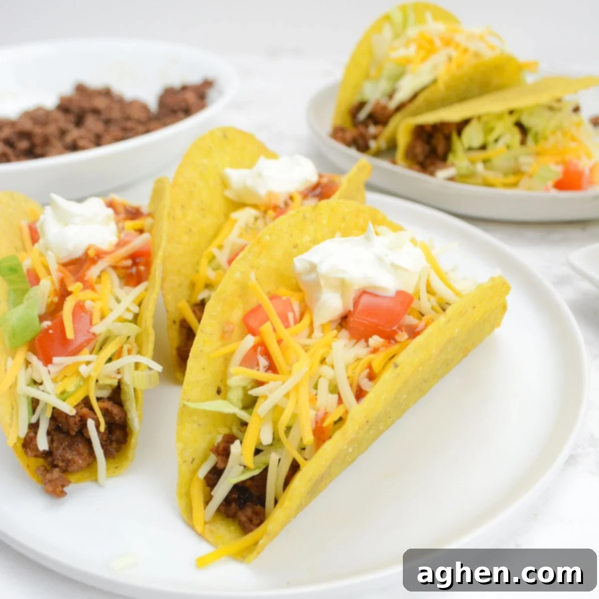 The Backyard's Best: Blackstone Tacos 2 A white plate with three fully assembled tacos. In the background is a smaller plate with two additional tacos and a bowl of taco meat.