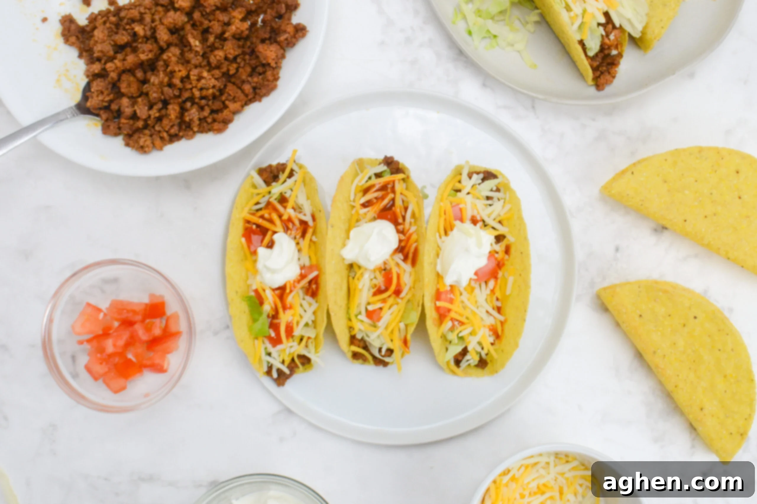 The Backyard's Best: Blackstone Tacos 7 An overhead of three tacos on a white plate. To the side sits the bowl of cooked meat, additional shells, and small bowls filled with toppings.
