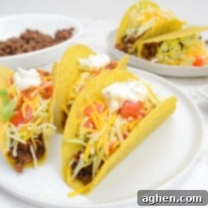 The Backyard's Best: Blackstone Tacos 8 A white plate with three fully assembled tacos. In the background is a smaller plate with two additional tacos and a bowl of taco meat.