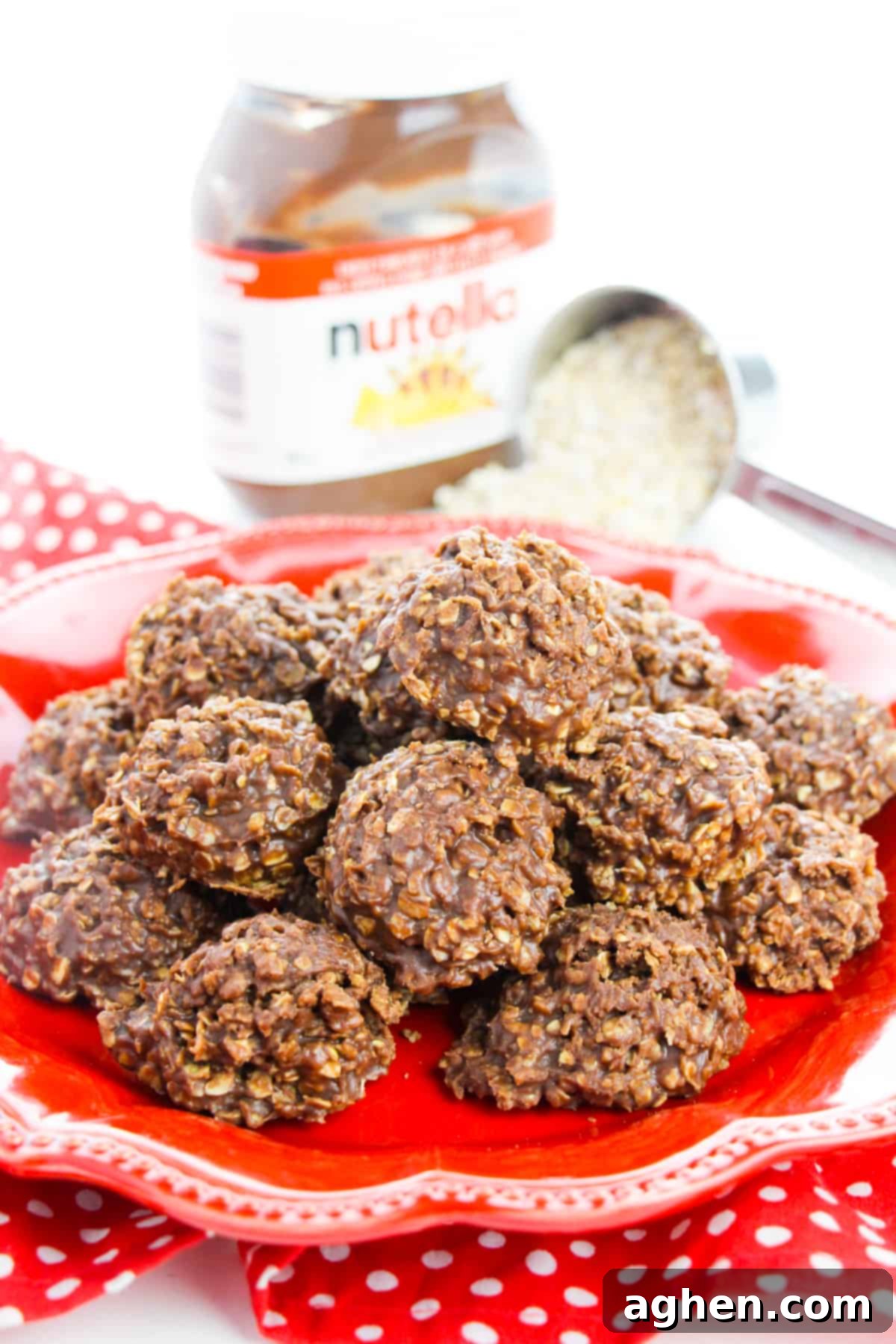 Delicious no-bake Nutella cookies piled high on a vibrant red plate, with a scoop of quick oats and a jar of Nutella spread subtly in the background, hinting at the simple, key ingredients.