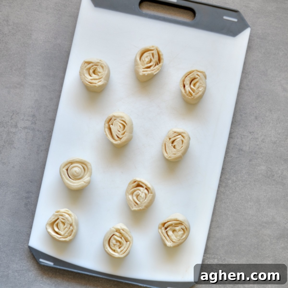 A log of crescent roll dough on a cutting board, being cut into equal pieces with a knife.