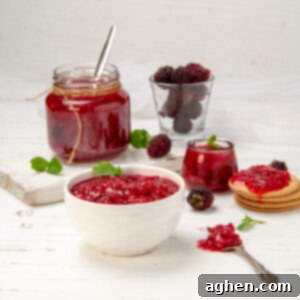 Easy homemade Apple Blackberry Jam in a dish with a spoon. A jar of extra jam is behind.