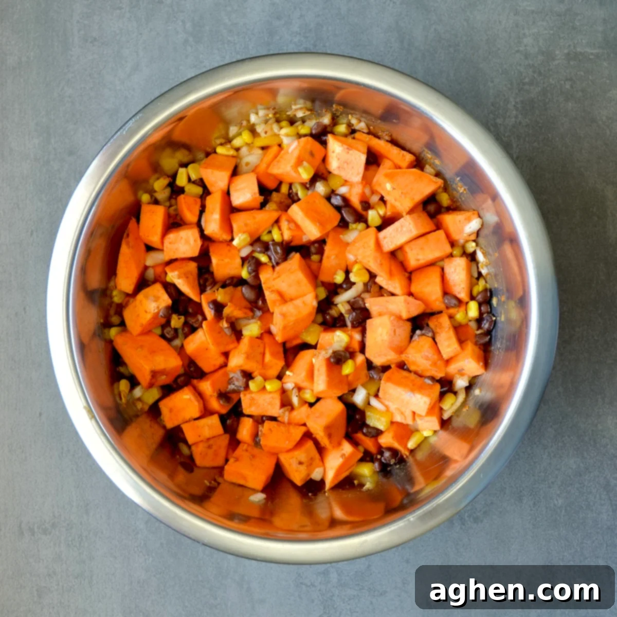 A large bowl containing sweet potatoes, onions, bell peppers, black beans, corn, and taco seasoning being mixed.
