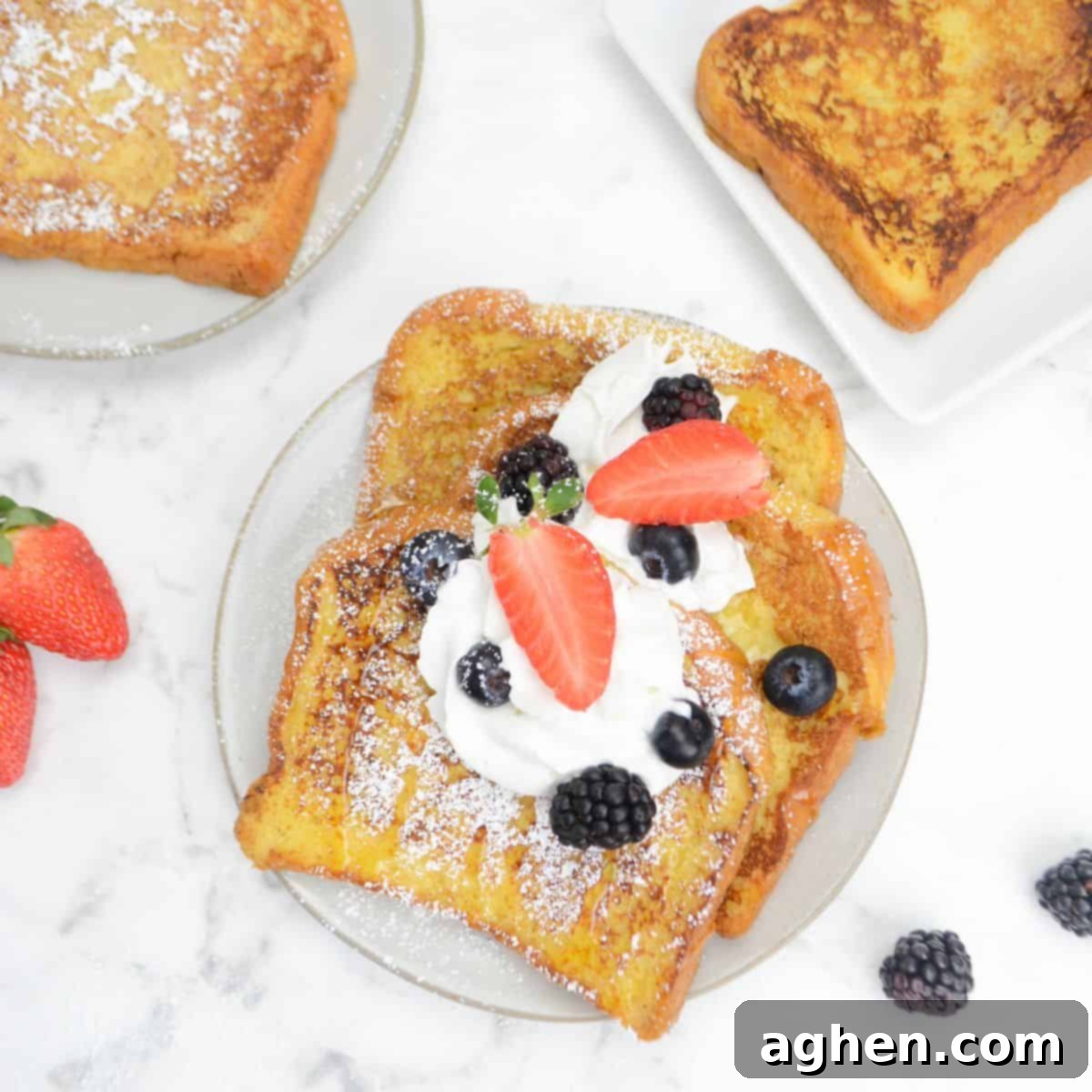 A plate filled with three slices French toast topped with whipped cream, berries, and powdered sugar. Two plates and berries sit to the side.