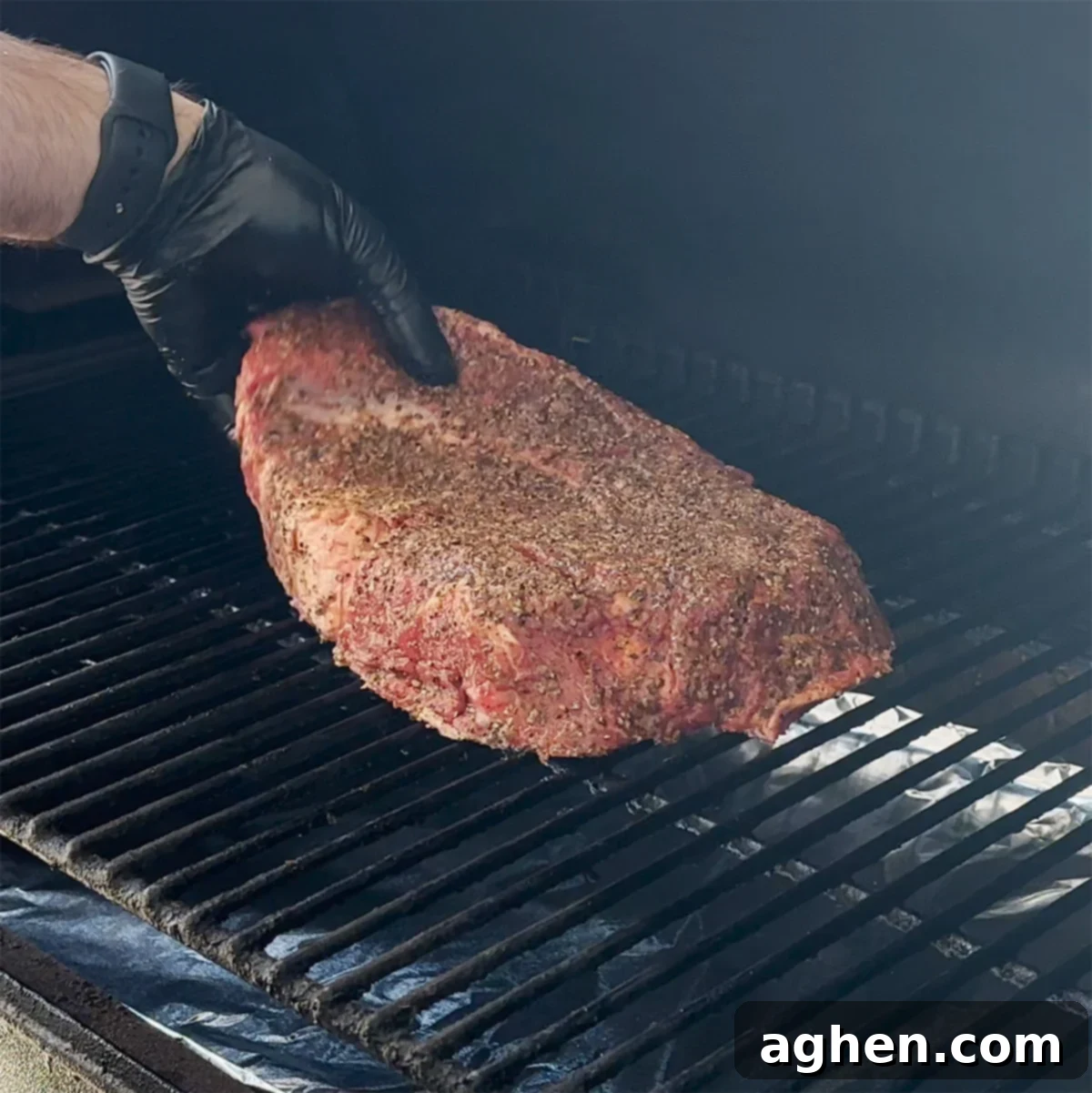 A chuck roast smoking on the grill grates of a Traeger, surrounded by visible smoke.
