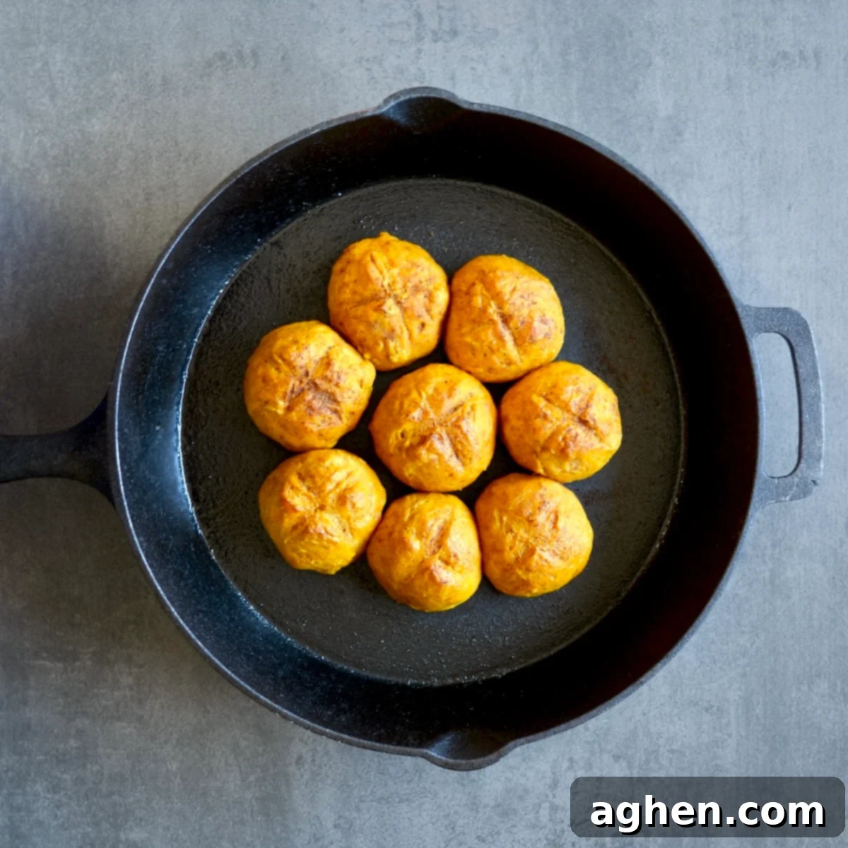 Golden-brown baked pumpkin dinner rolls fresh out of the oven in a cast iron skillet