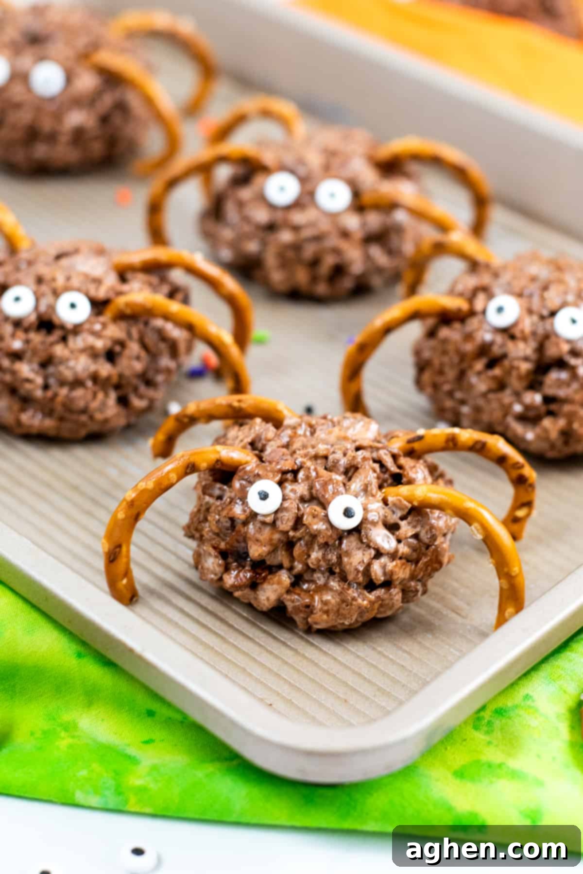 Frightfully Delicious Spider Bites 3 Round chocolate rice cereal treats with pretzel legs and candy eyes, arranged on a serving platter.