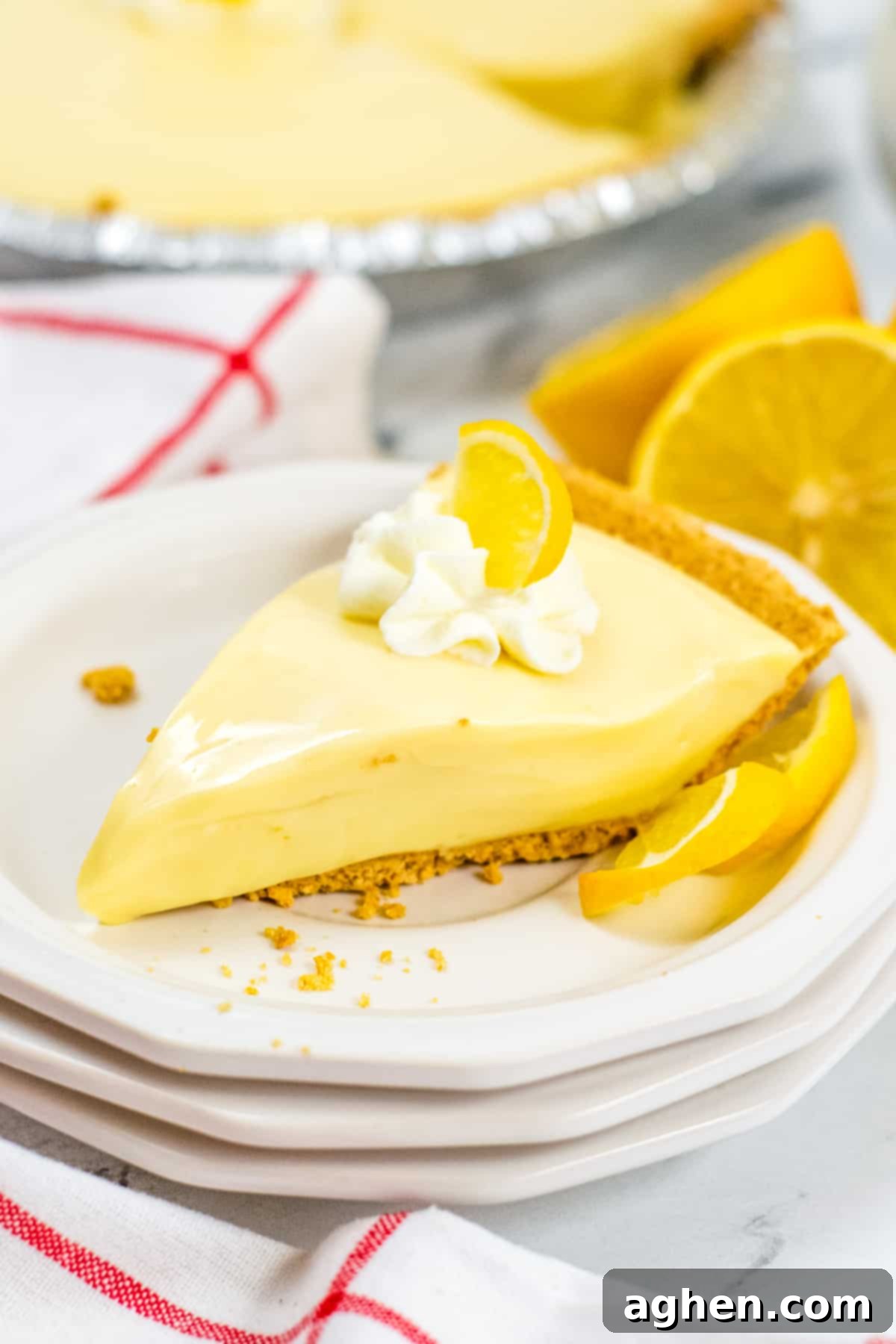 Zesty Lemon Icebox Pie 2 Lemon Icebox Pie slice on stack of white plates. Pie is topped with dollop of whipped cream and slice of lemon. Whole pie can be seen in background, as well as fresh lemons