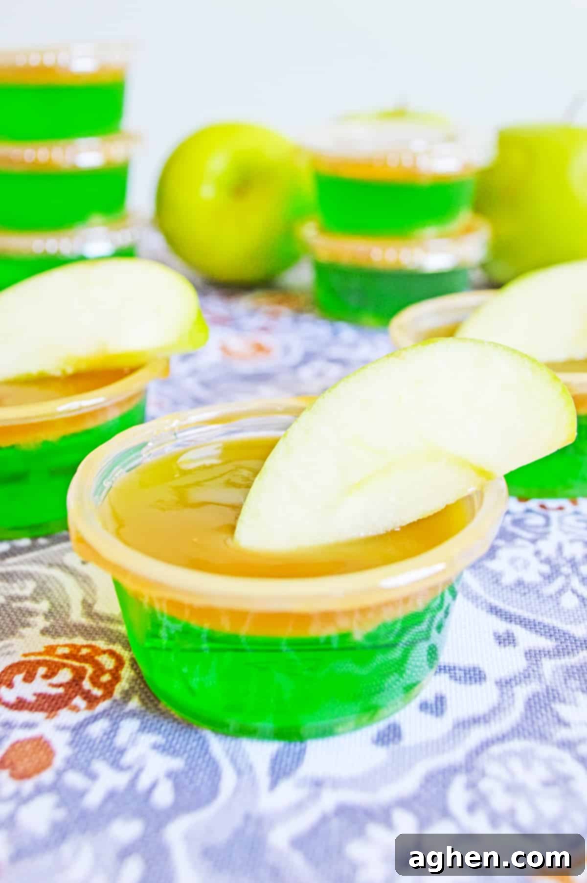 Caramel Apple Jello Shot in plastic shot glass with caramel topping and garnished with apple wedge.