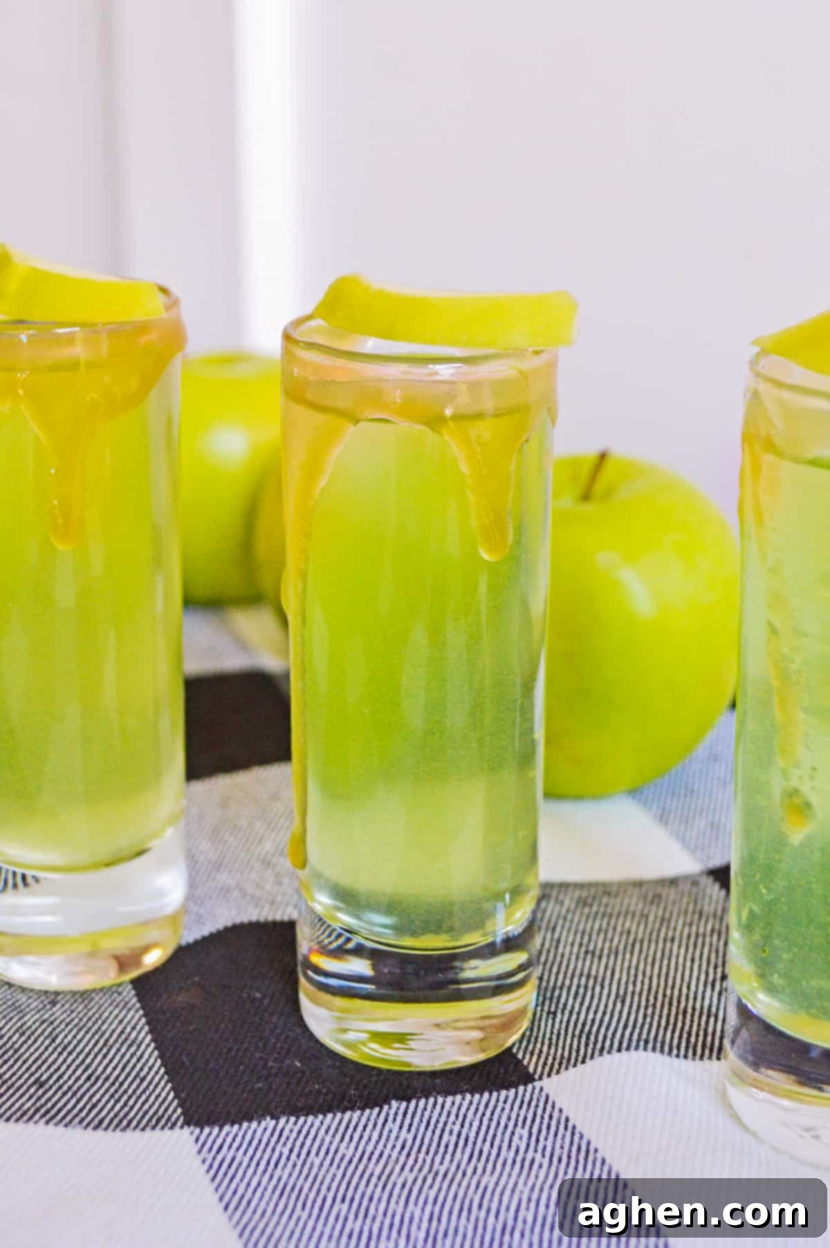 Decadent Caramel Apple Shots 2 Caramel apple shots with caramel vodka, apple cider, and sour apple mixer, garnished with an apple slice and caramel drizzle.