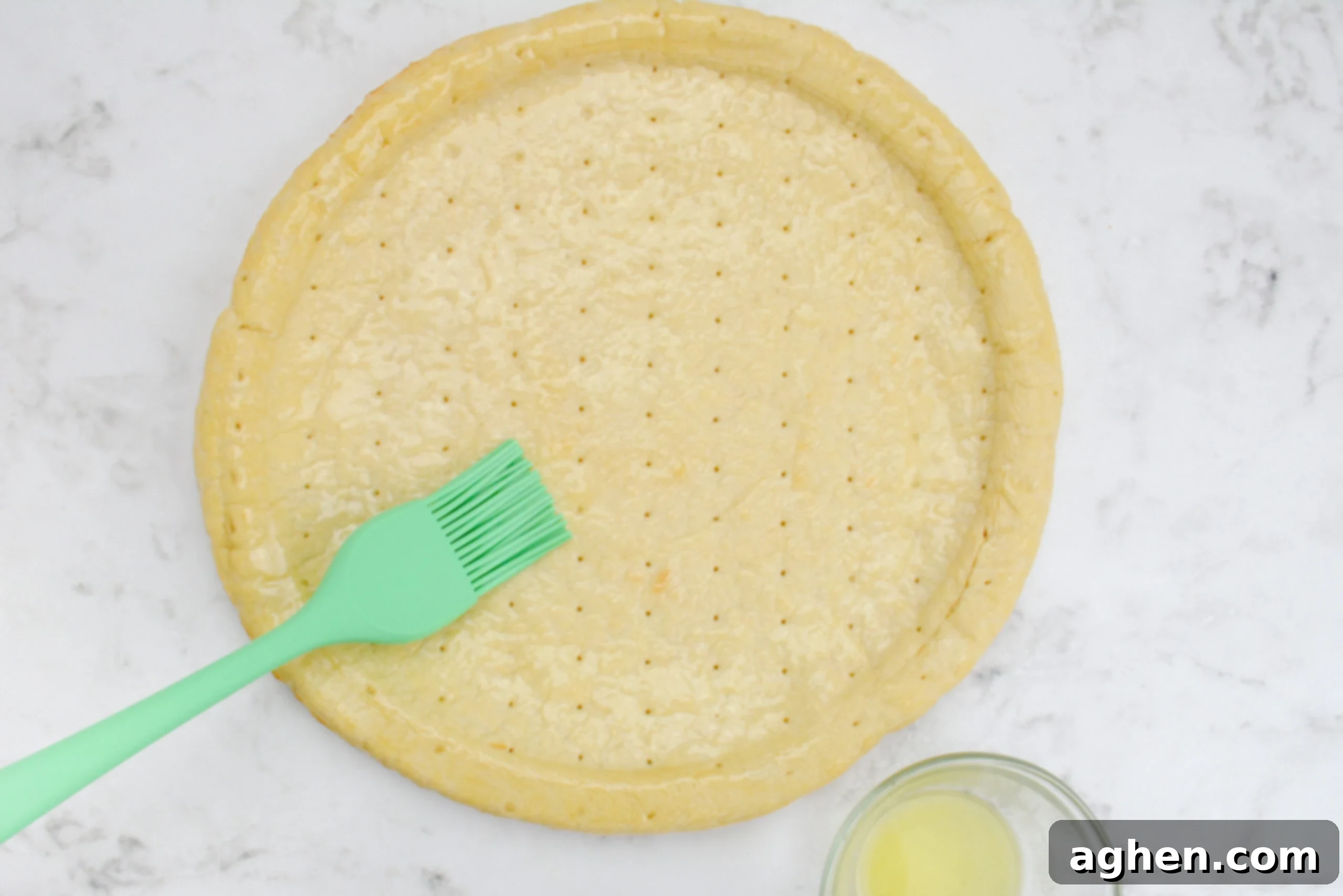 An overview view of a green pastry brush adding butter to the crust.
