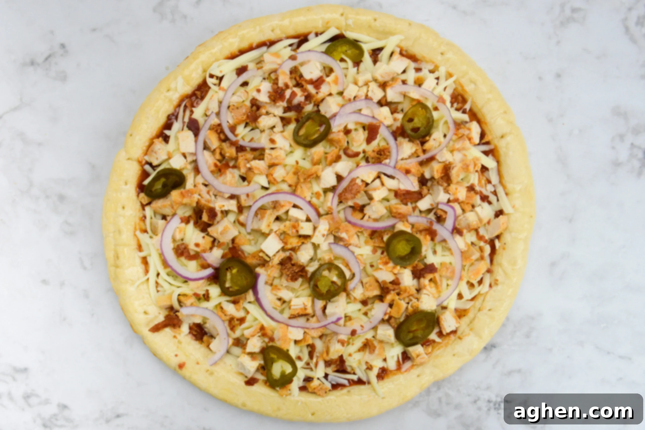 An overhead view of the assembled but uncooked pizza complete with onions and sliced jalapenos.