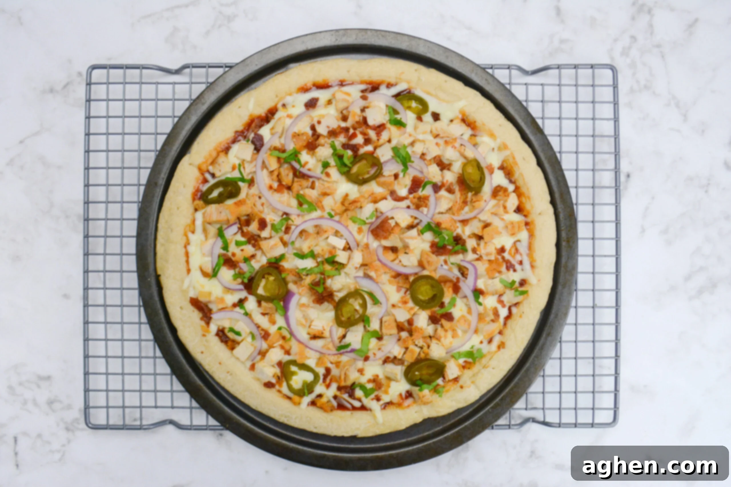 The cooked and finished pizza is shown on a grey cooling rack on a white marble background.