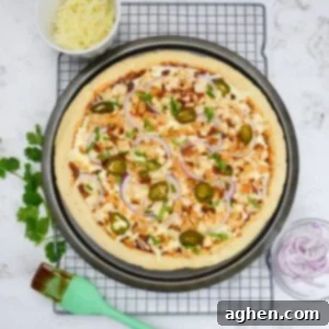 The cooked pizza is on a cooling rack and surrounded by small bowls with onions and cheese. Additional cilantro is placed to the side and a pastry brush with barbecue sauce is placed to the side.