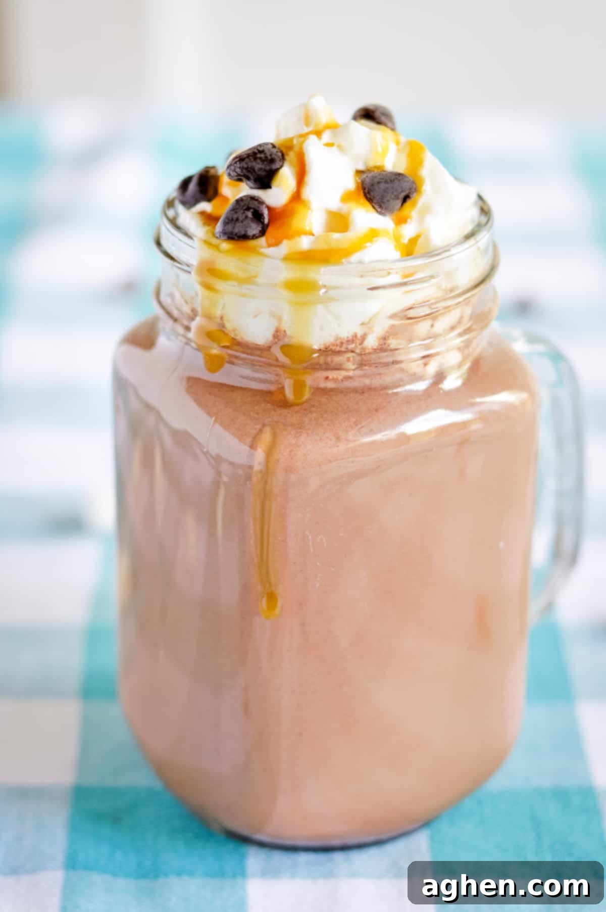 Hot chocolate in a glass mason jar mug topped with whipped cream, caramel sauce, and chocolate chips