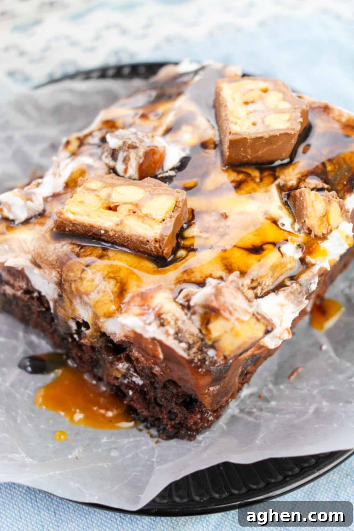 Overhead view of a Snickers chocolate poke cake in a 9x13 pan, topped with whipped cream, chocolate sauce, and caramel sauce drizzles.