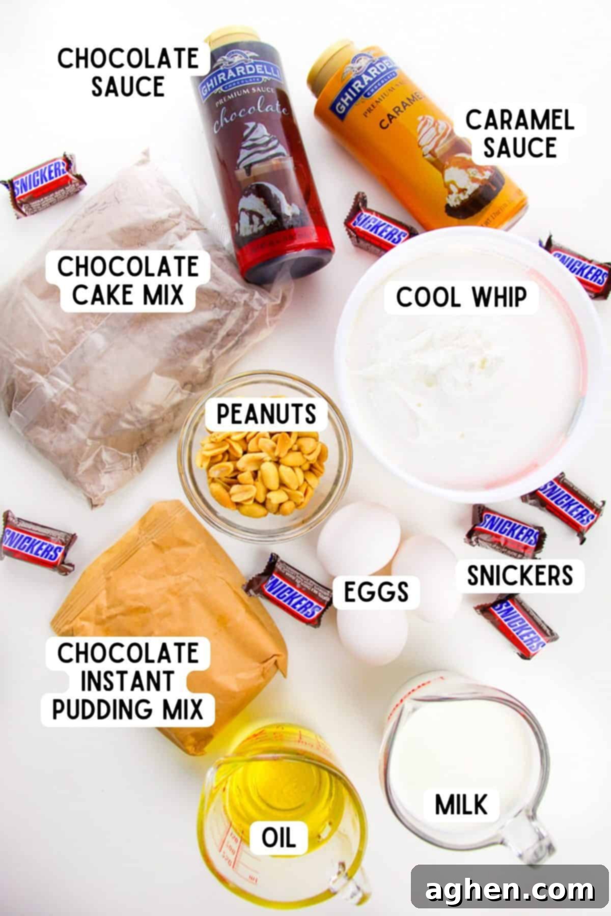 Assorted ingredients for Snickers Poke Cake laid out: chocolate cake mix box, instant chocolate pudding mix, milk, caramel sauce, chocolate sauce, peanuts, Cool Whip container, and Snickers bars.