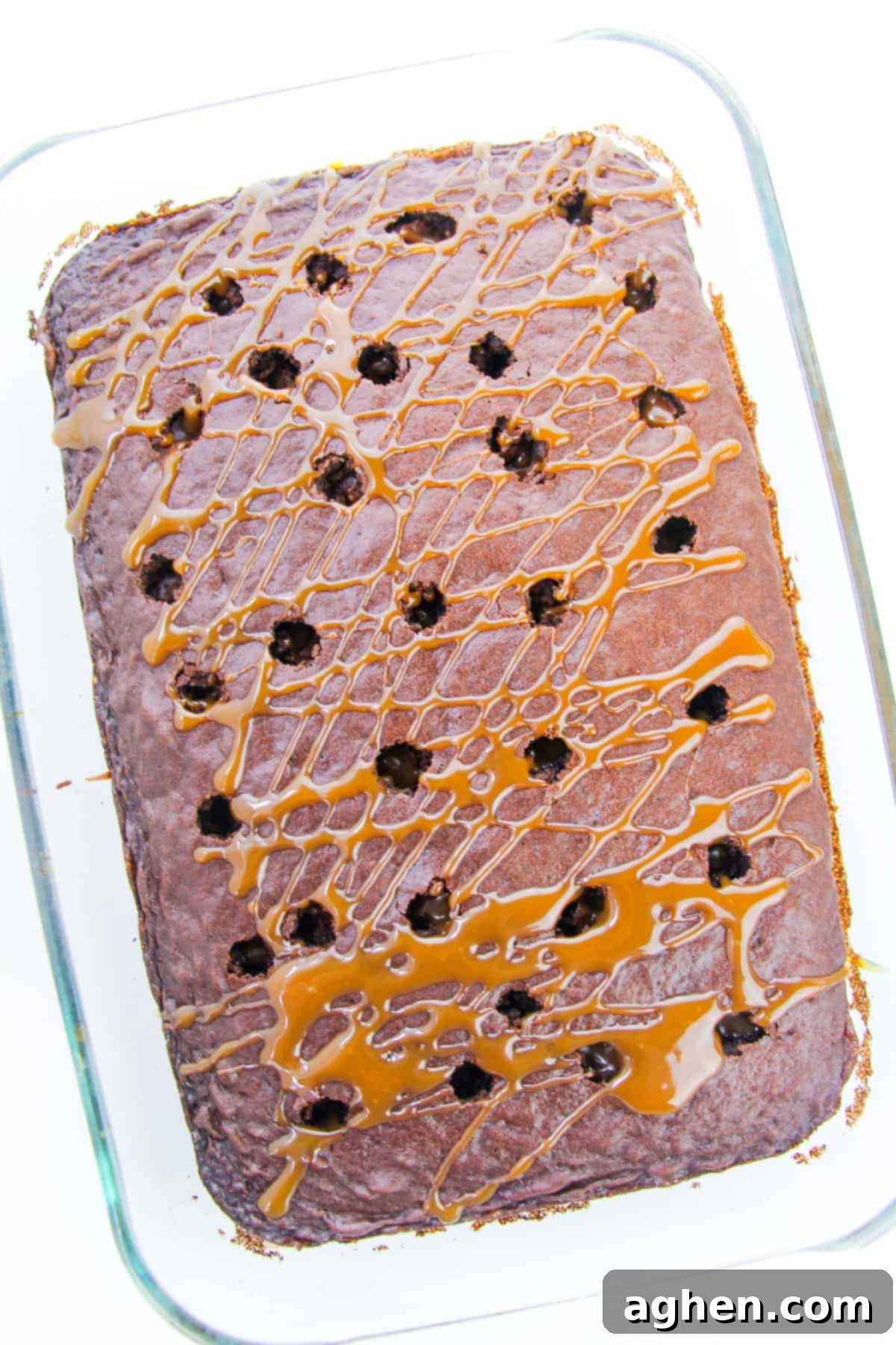 Chocolate poke cake in a 9x13 pan with caramel sauce being drizzled over the top, visibly seeping into the poked holes.