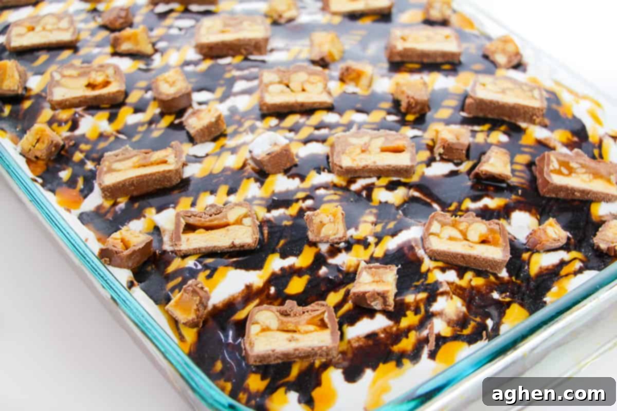 Close-up of a full sheet cake with Cool Whip, caramel, chocolate sauce, and scattered Snickers candy pieces, ready to be served.