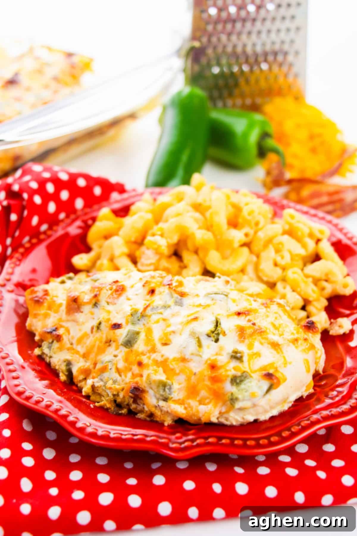 Plated jalapeño popper chicken breast with a side of macaroni and cheese, fresh jalapeño peppers, and shredded cheese in the background.